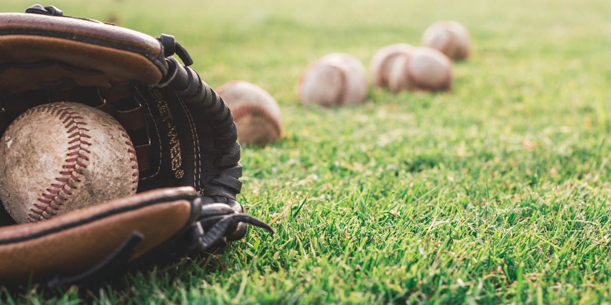Close-up of a baseball glove with balls on a green field