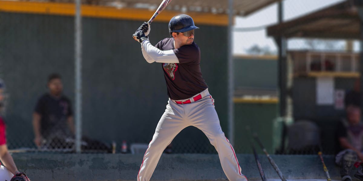 A young baseball player wearing a helmet dodges a pitch on a sunny day during a game.