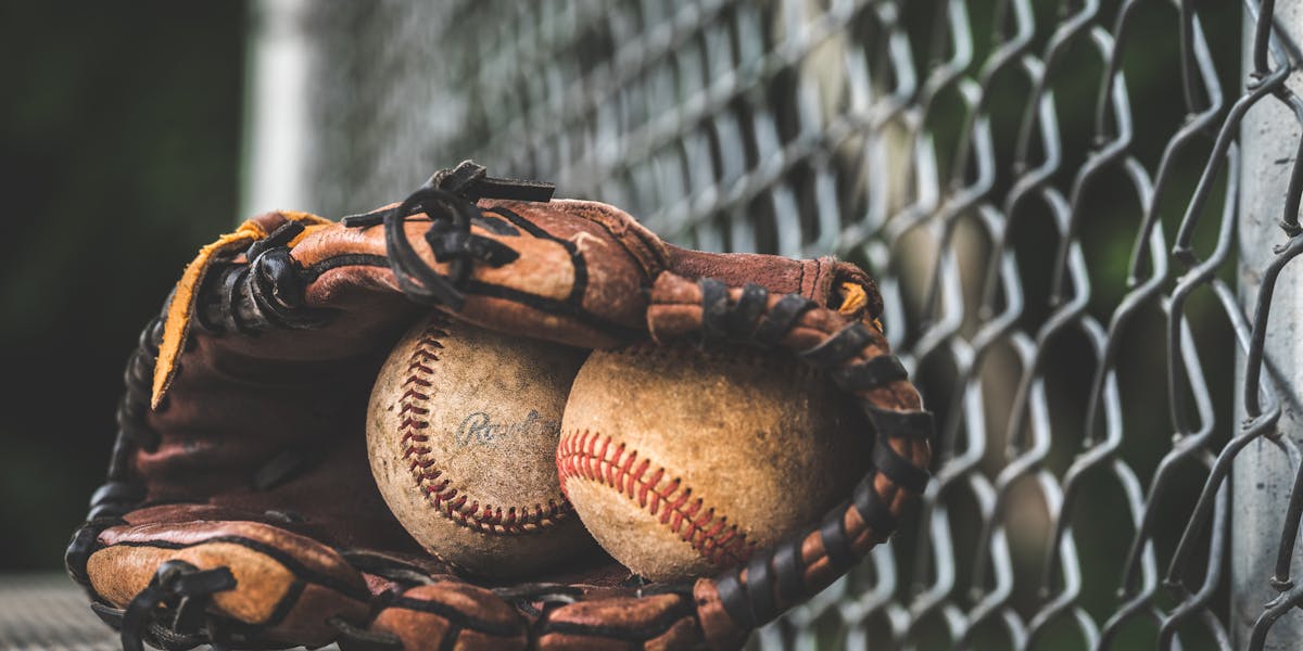 Close-up of a leather glove holding two vintage baseballs, resting near a chain-li...