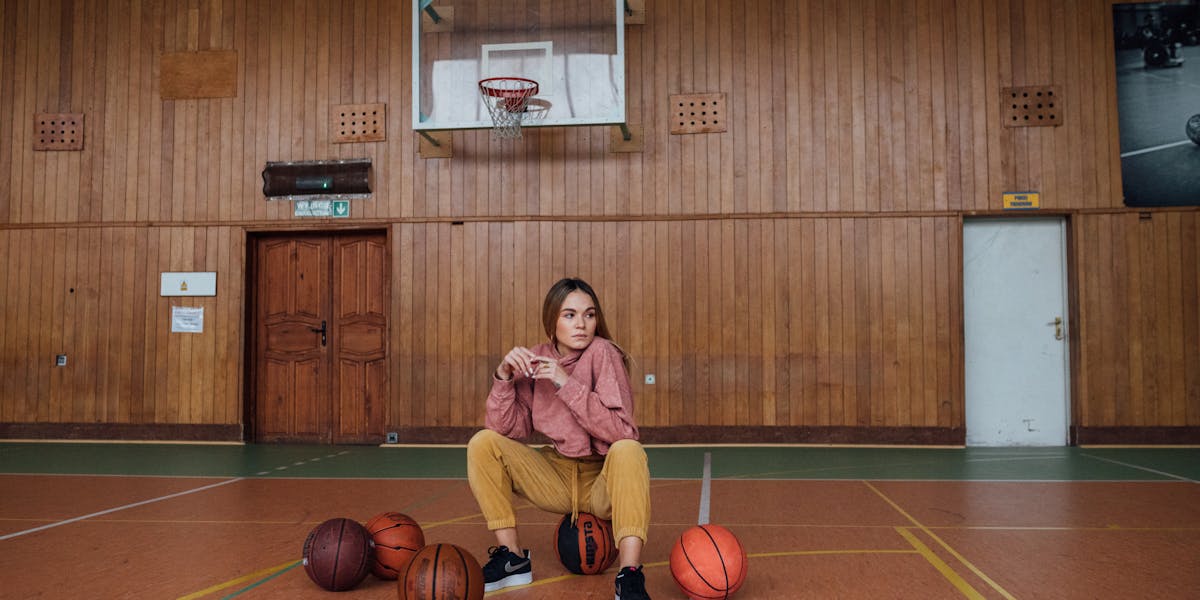 A young woman poses confidently in an indoor basketball court, surrounded by baske...