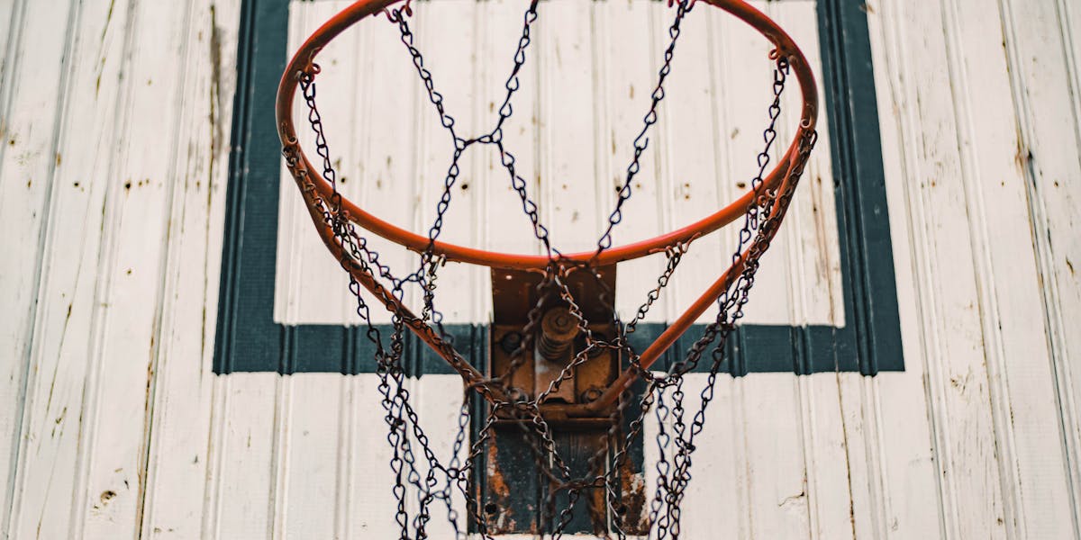A low-angle view of a basketball hoop with a chain net against a bright blue sky.