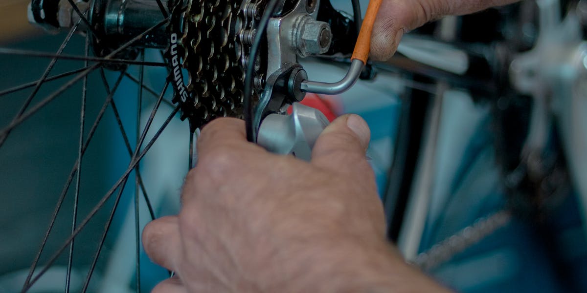 Hands working on bicycle gear in a workshop, showcasing repair tools.