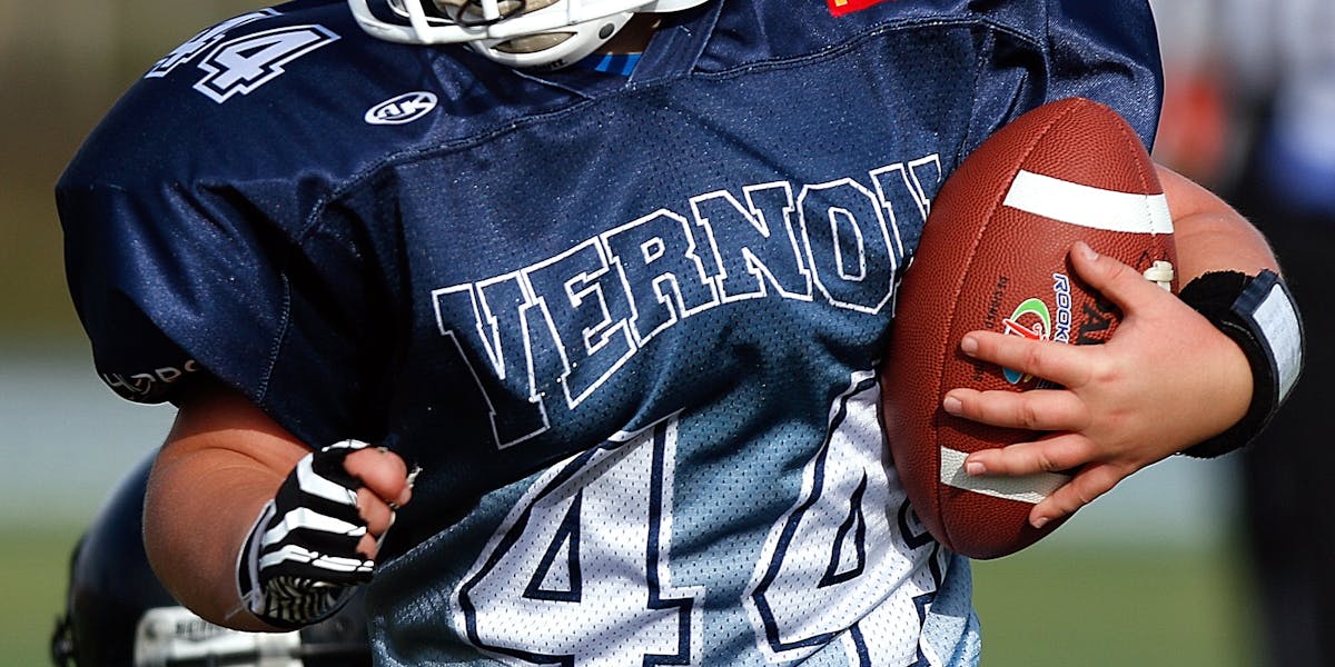 A young child in football gear holding a ball during a game on the field.