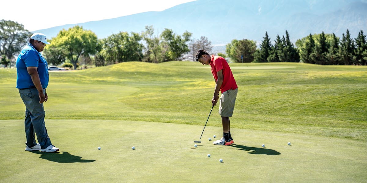 Two men practicing putting on a sunny golf course with mountain views.