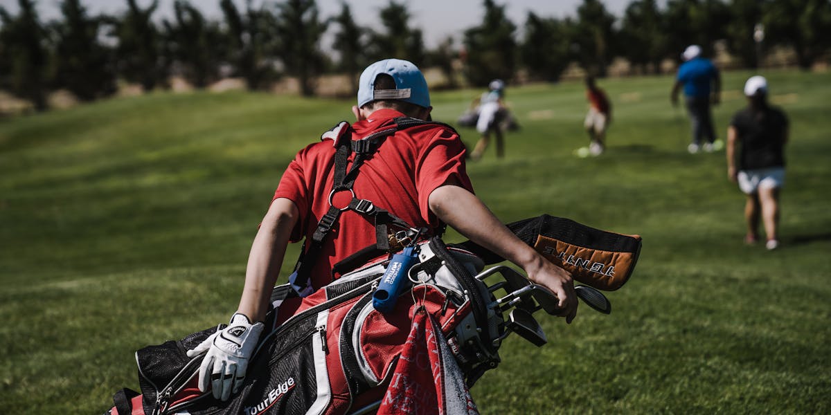 Woman golfer in red polo shirt and hat standing with a golf club under palm tree