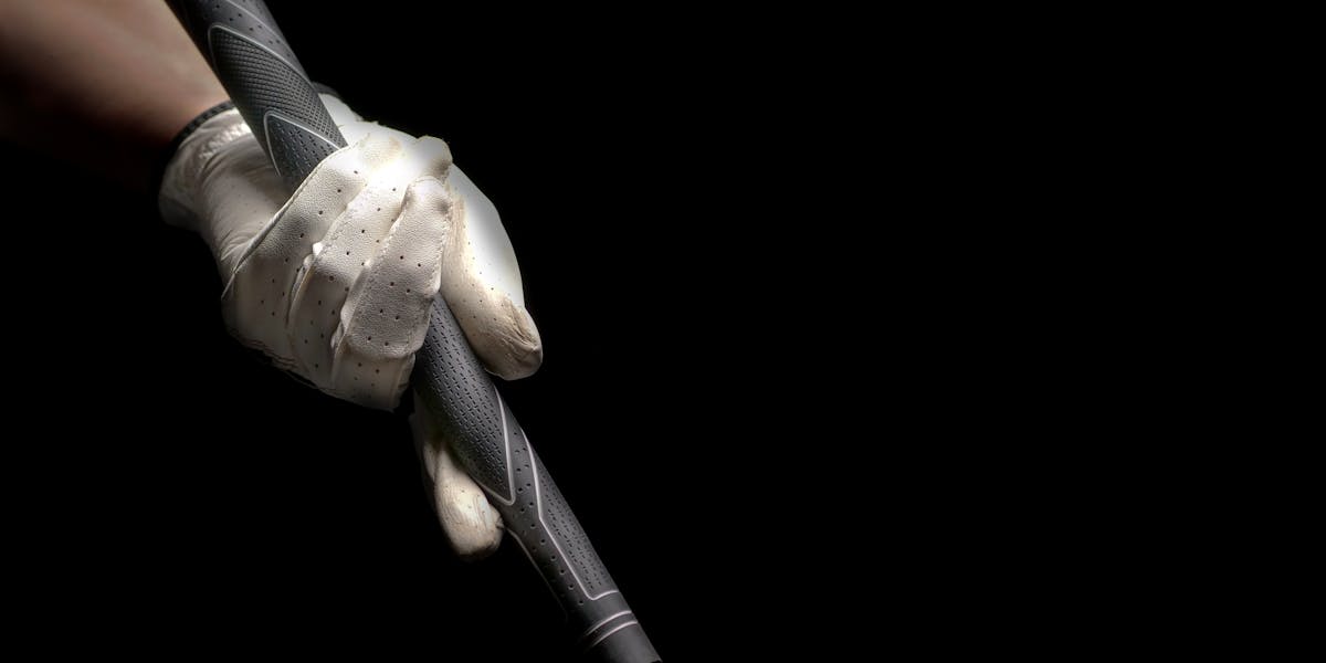 Golf glove hand gripping a club against a black backdrop, showcasing sports focu