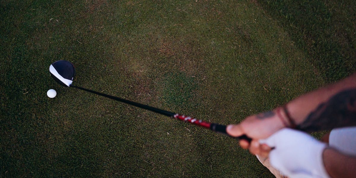 Golfer preparing to swing on a lush course, showing glove and tattoo.