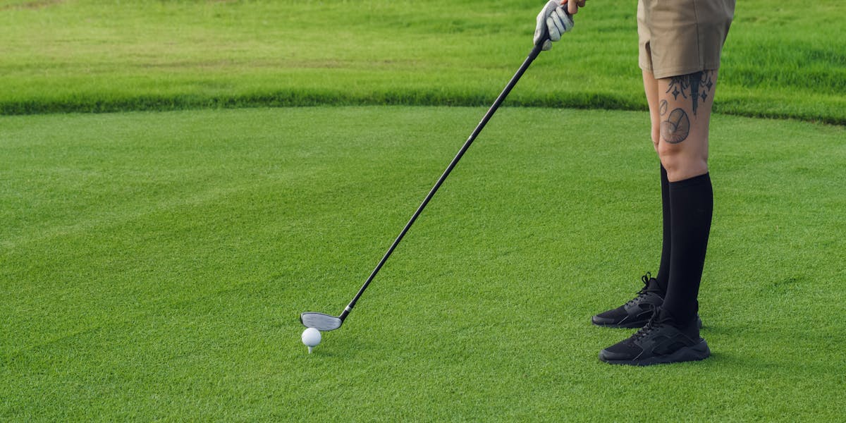 Close-up view of a golfer ready to swing with a club on a lush green grass field.