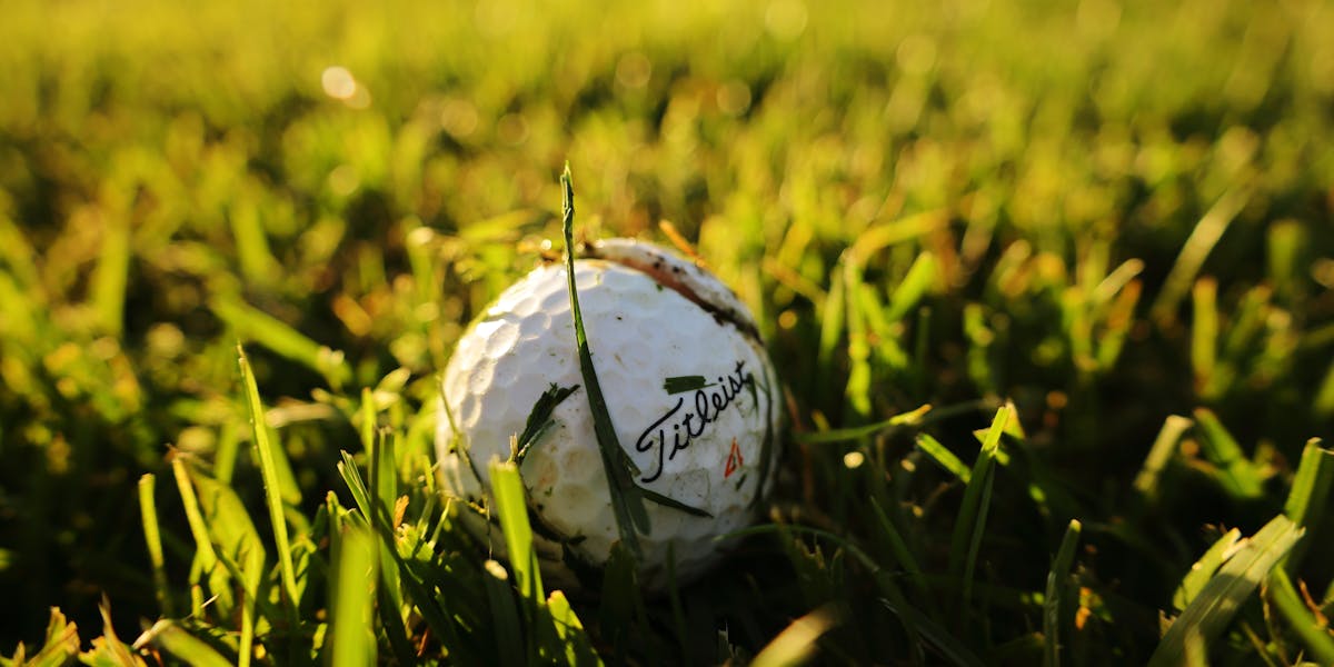 A close-up shot of a golf ball nestled in vibrant green grass, perfect for sports-...