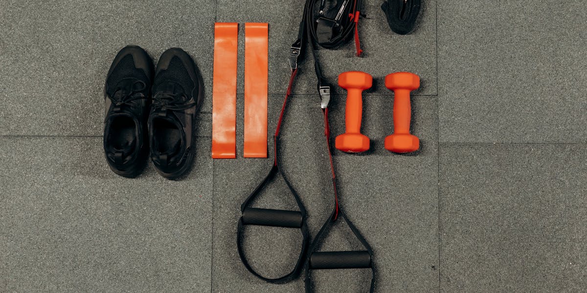 Flat lay of fitness gear including dumbbells, sneakers, and resistance bands for a...