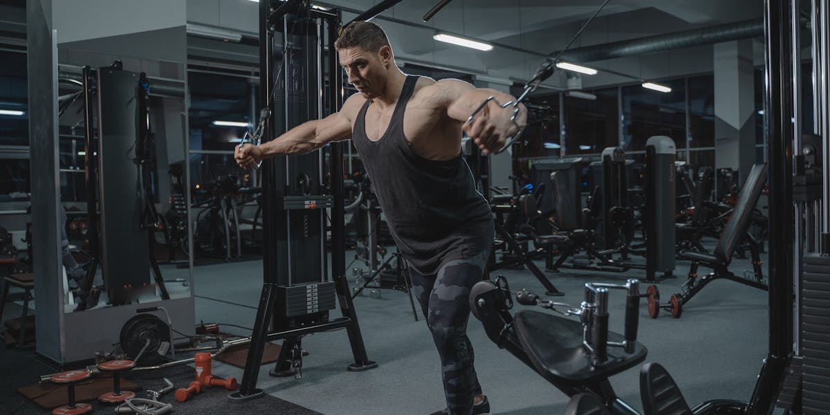 Muscular man working out in the gym using a cable crossover machine.