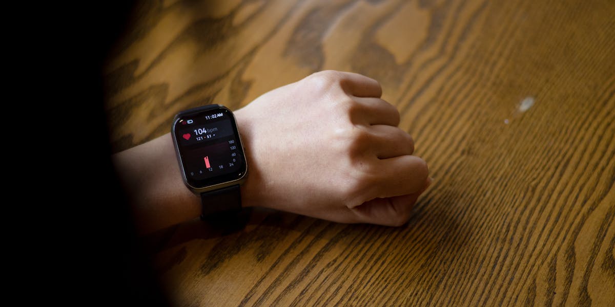 A person checks heart rate on smartwatch showing 104 bpm on wooden table.