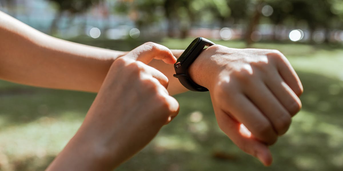 A person interacts with a smartwatch in a sunny park, emphasizing fitness and te
