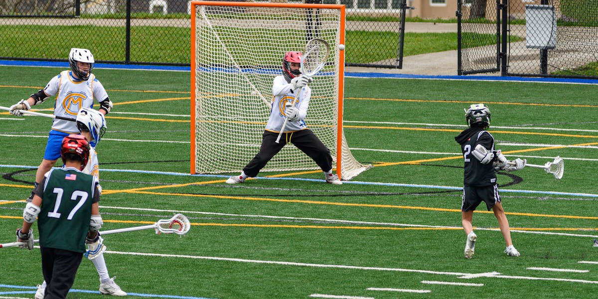Action-packed youth lacrosse game with players in full gear on a green field.