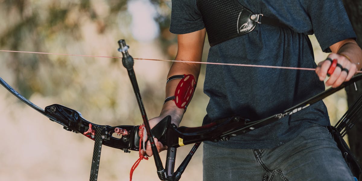 A person equipped with archery gear outdoors, holding a recurve bow ready to shoot.