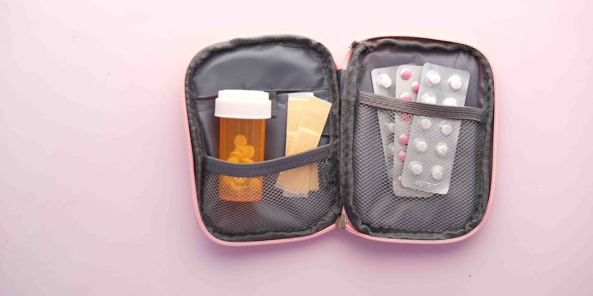 Open first aid kit with pill bottle, blister packs, and band-aids on a pastel back...