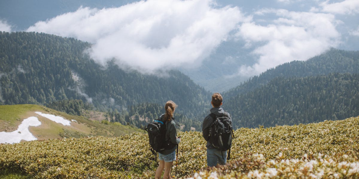 Two hikers with backpacks admire a stunning mountain landscape. Perfect for travel...