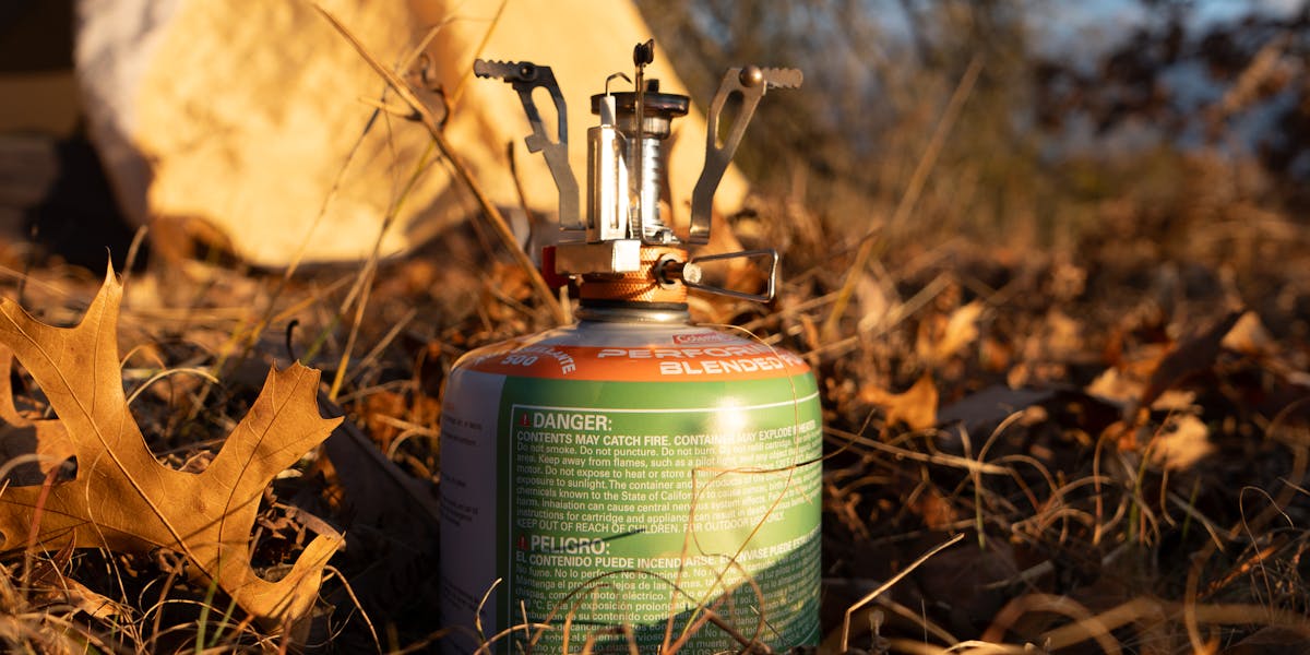 Portable camping stove set up amidst autumn leaves next to a tent outdoors.