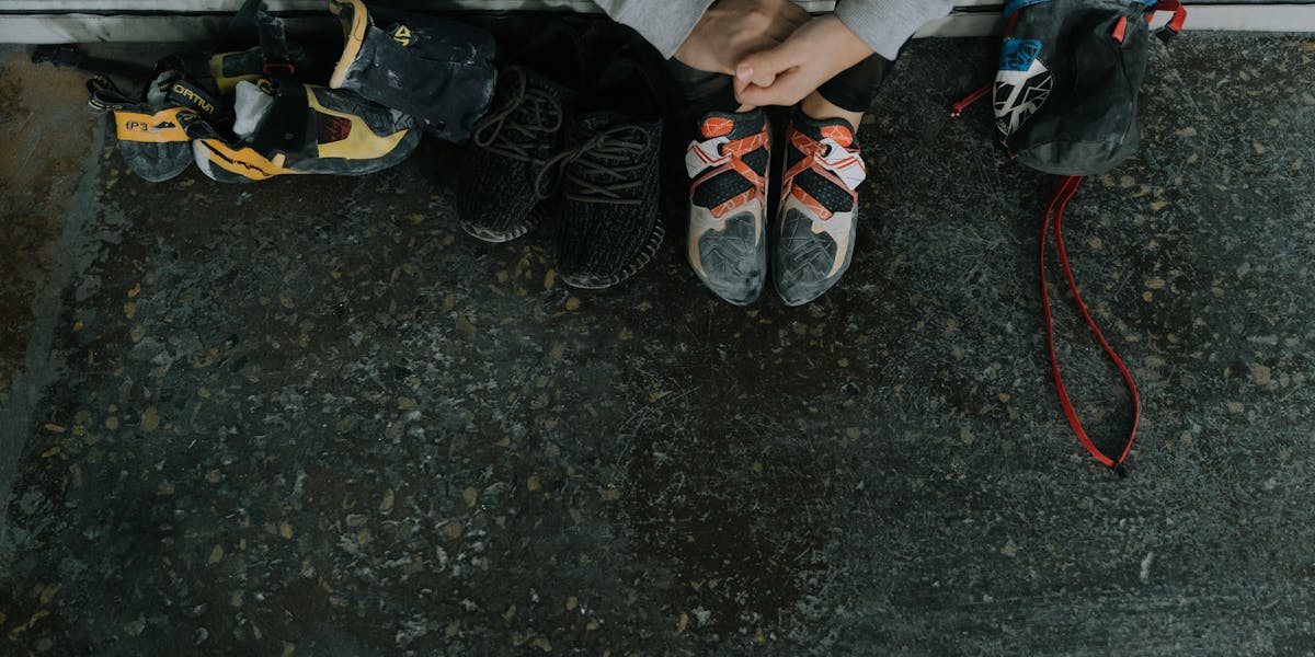 An overhead view of rock climbing shoes, chalk bag, and sneakers on a gym floor.