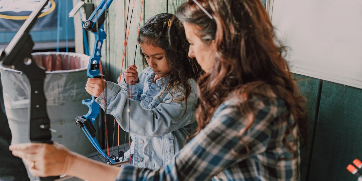 A woman holding a compound bow aims during archery practice indoors, showcasing 