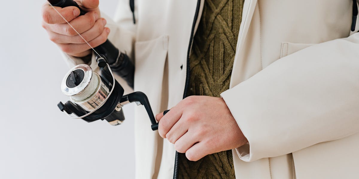 Close-up of hands holding a fishing rod and reel, focusing on fishing equipment.