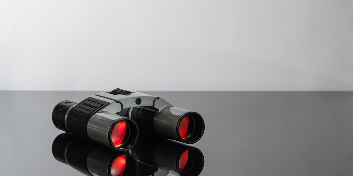 Close-up of modern binoculars with red lenses reflecting on a sleek glass surfac