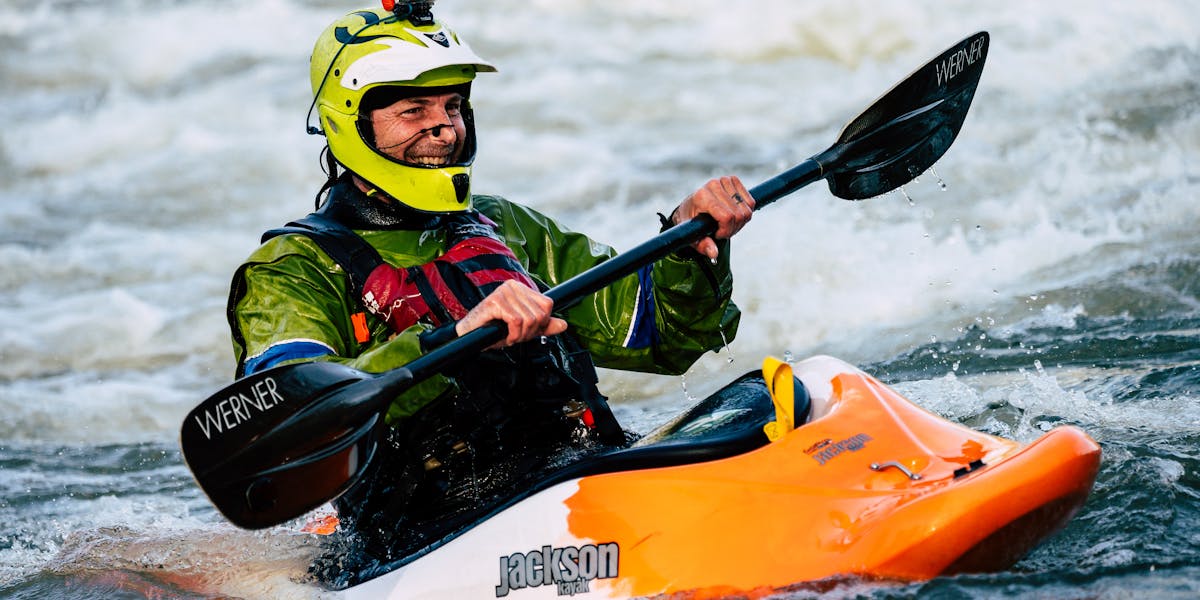 An adventurous kayaker smiles while paddling through wild whitewater rapids.