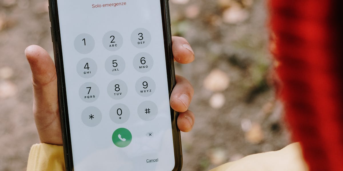 Close-up of a person in a yellow jacket dialing 112 on a smartphone outdoors.