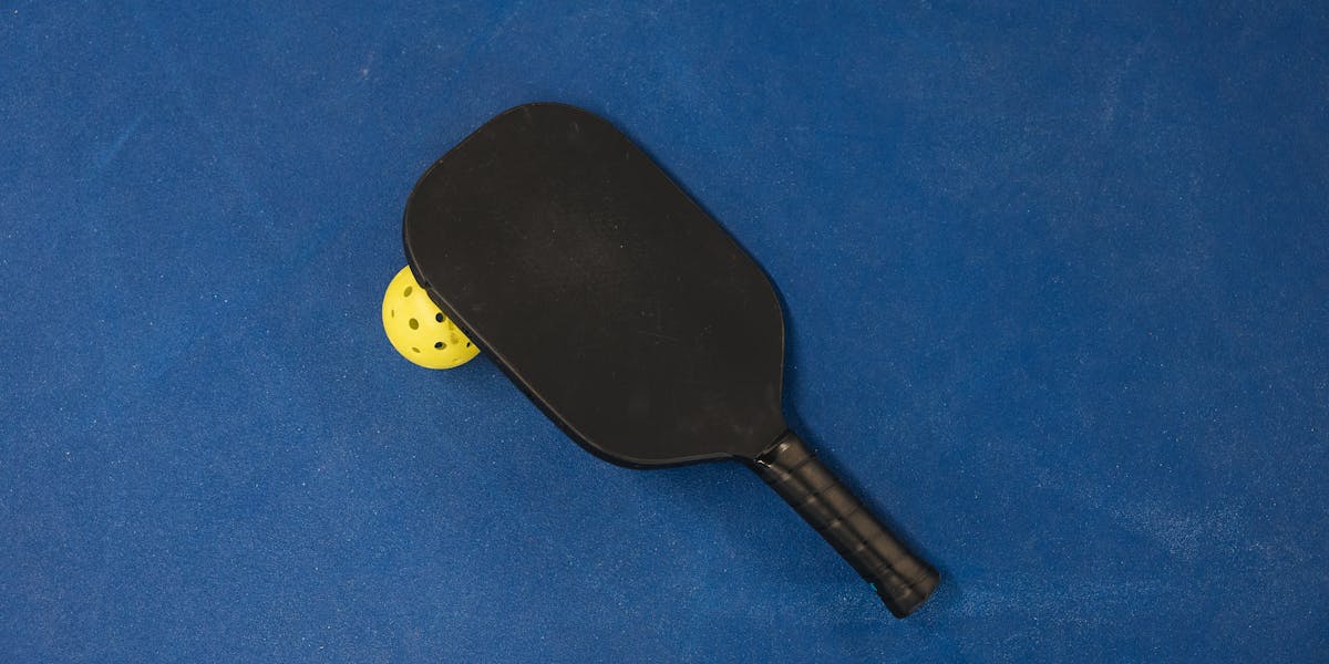 A pickleball paddle and ball on a textured blue surface, showcasing sports equipment.