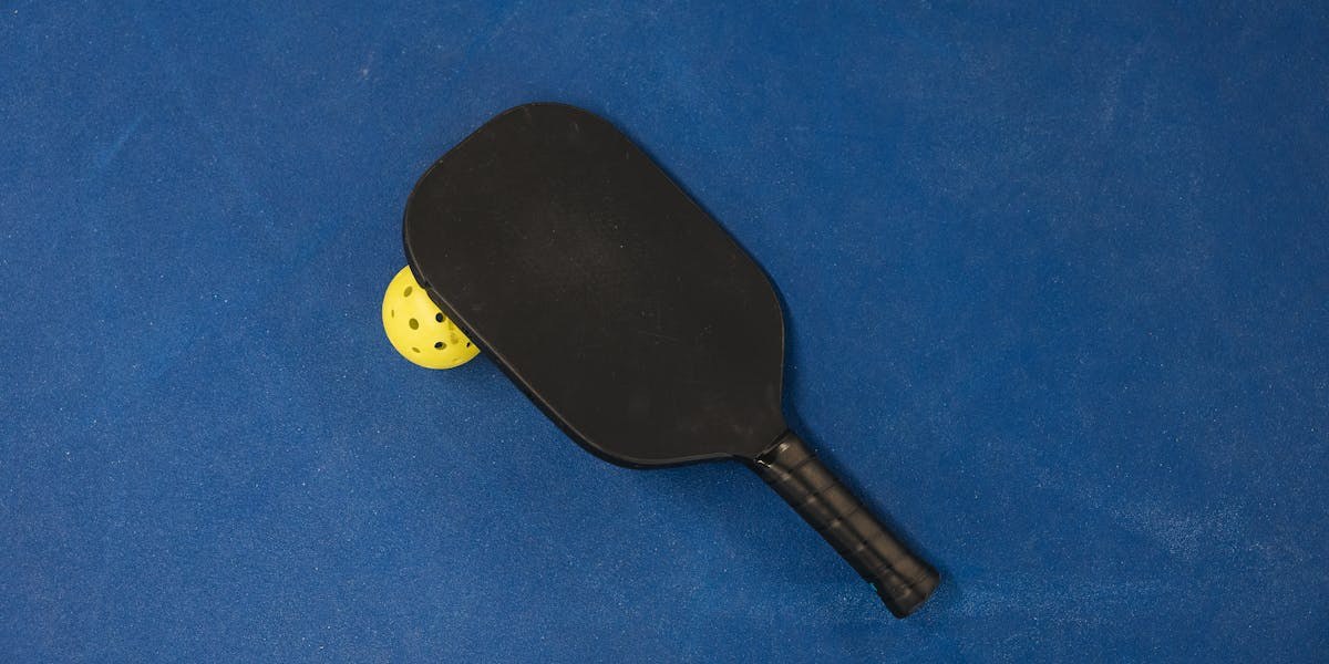 Pickleball paddle and ball on a blue court.