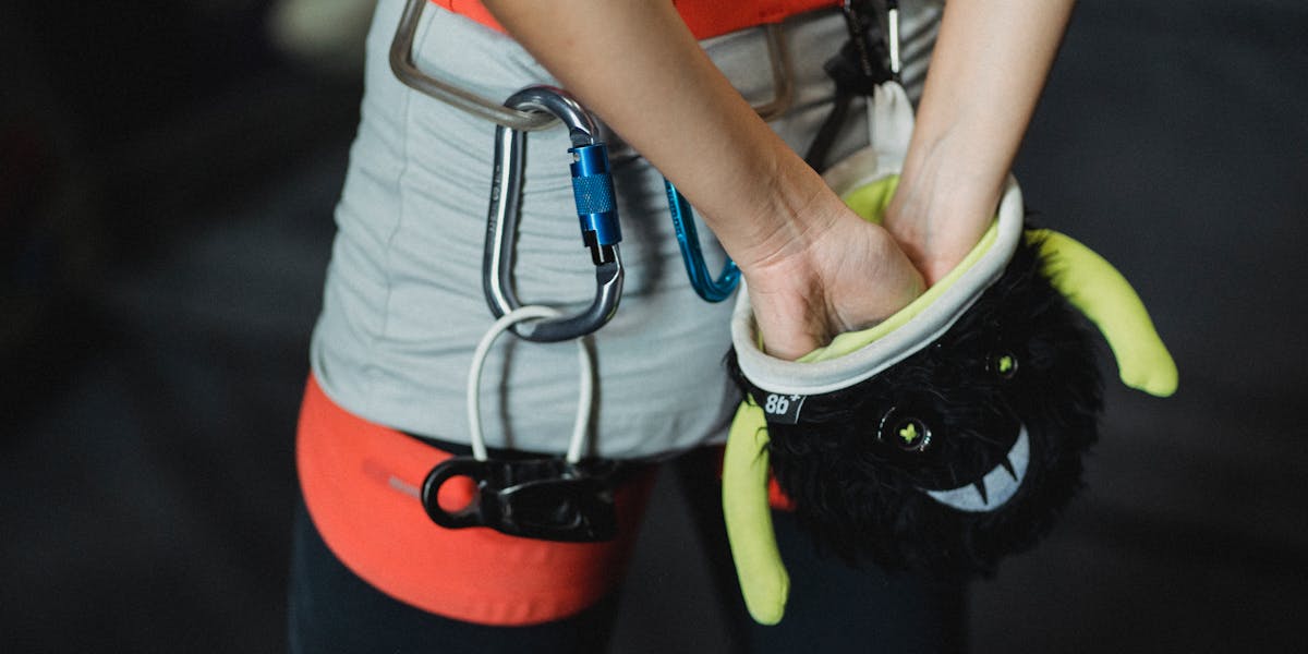 Back view of crop anonymous female climber in protective gear rubbing hands with c...