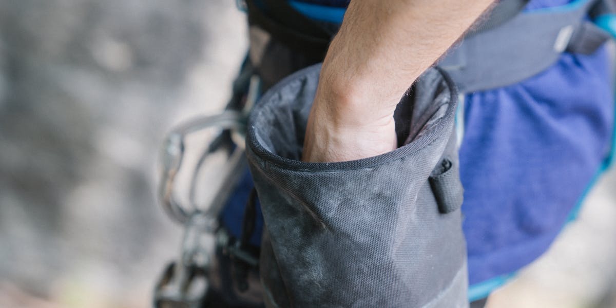 A climber's hand reaches into a chalk bag, highlighting climbing activity.