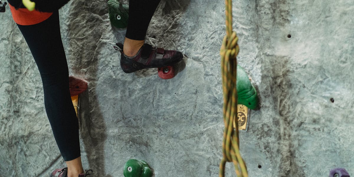 A climber's back showing harness, carabiners, and coiled rope in an outdoor sett