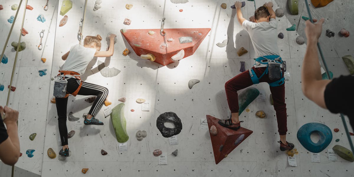 Two young climbers ascend an indoor rock wall, focused and determined.