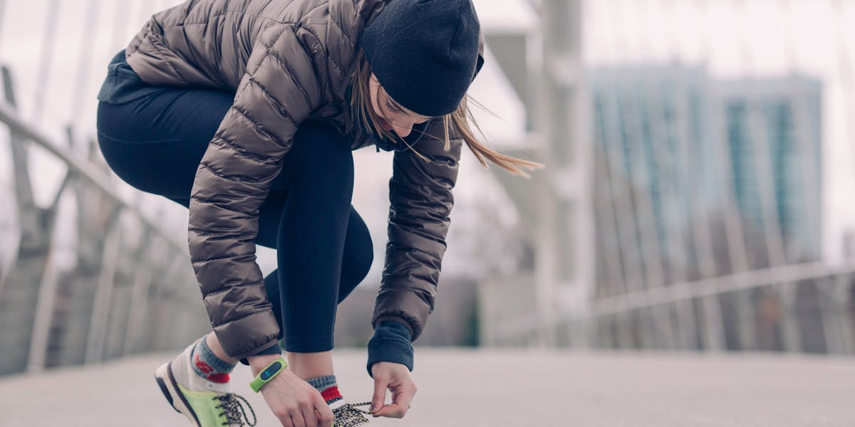 Woman in activewear tying running shoes on a city bridge, ready for a winter jog