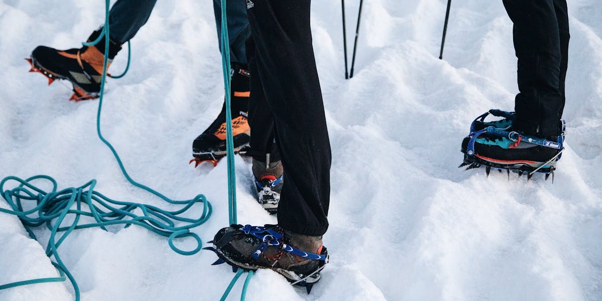 Mountaineering crampons attached to boots on snow with climbing rope nearby