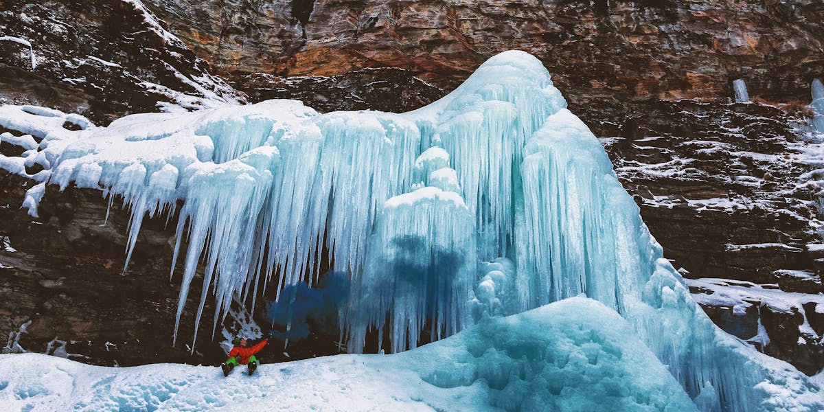 Daring ice climber tackles towering frozen waterfall in winter's icy embrace.