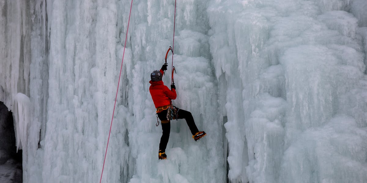 A climber in red jacket ascends a massive frozen waterfall, showcasing their ice