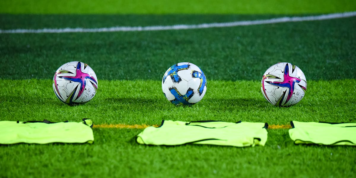Three soccer balls and training bibs on a lush green field in Rawalpindi, Pakistan.