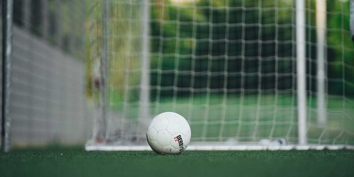 Close-up of soccer ball on outdoor field with goal net, perfect for sports themes.