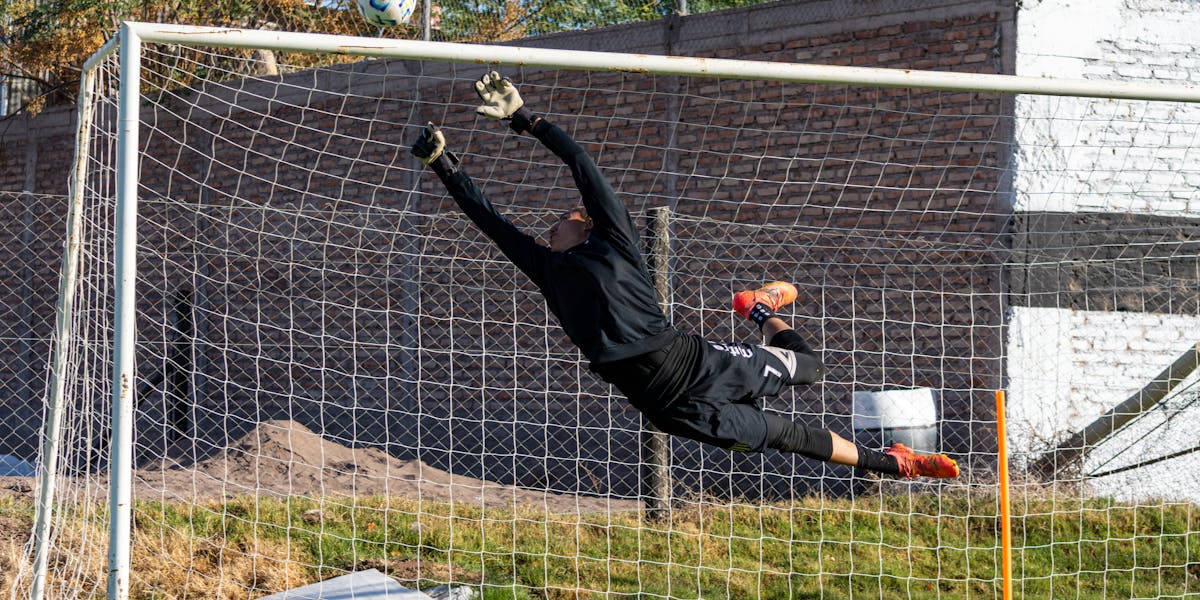 Dynamic action shot of a goalkeeper making a high save during a soccer game outd