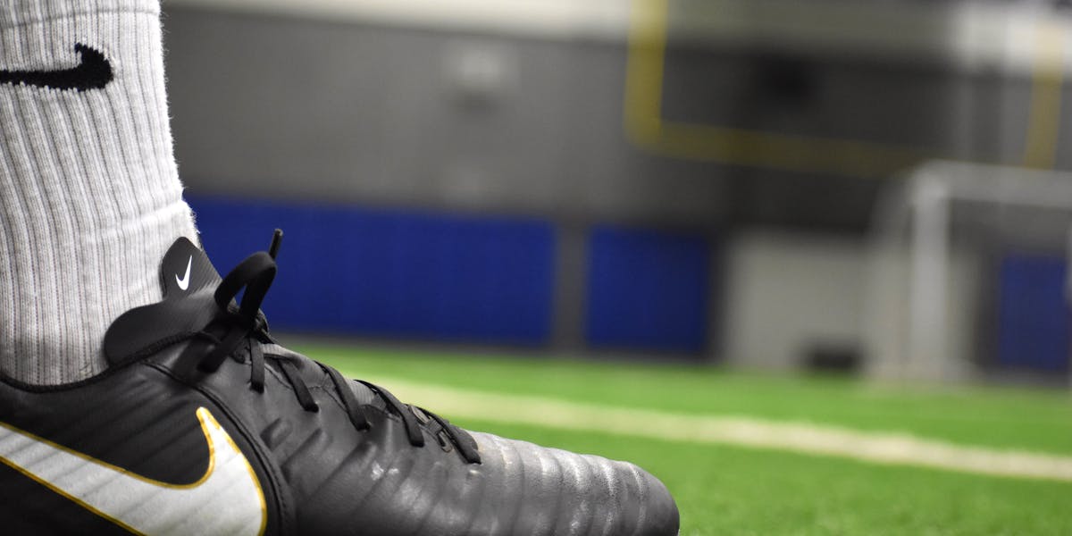 A detailed shot of a soccer cleat on an indoor turf field, emphasizing footwear an...