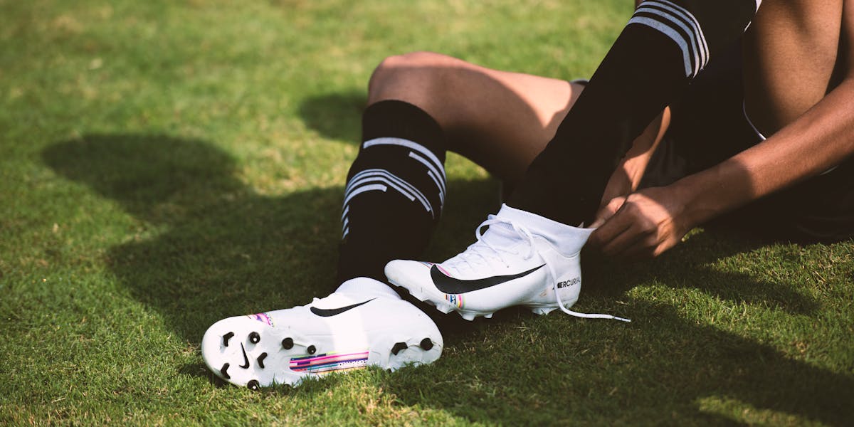 Close-up of a soccer player tying cleats on a sunny grass field, ready for action.