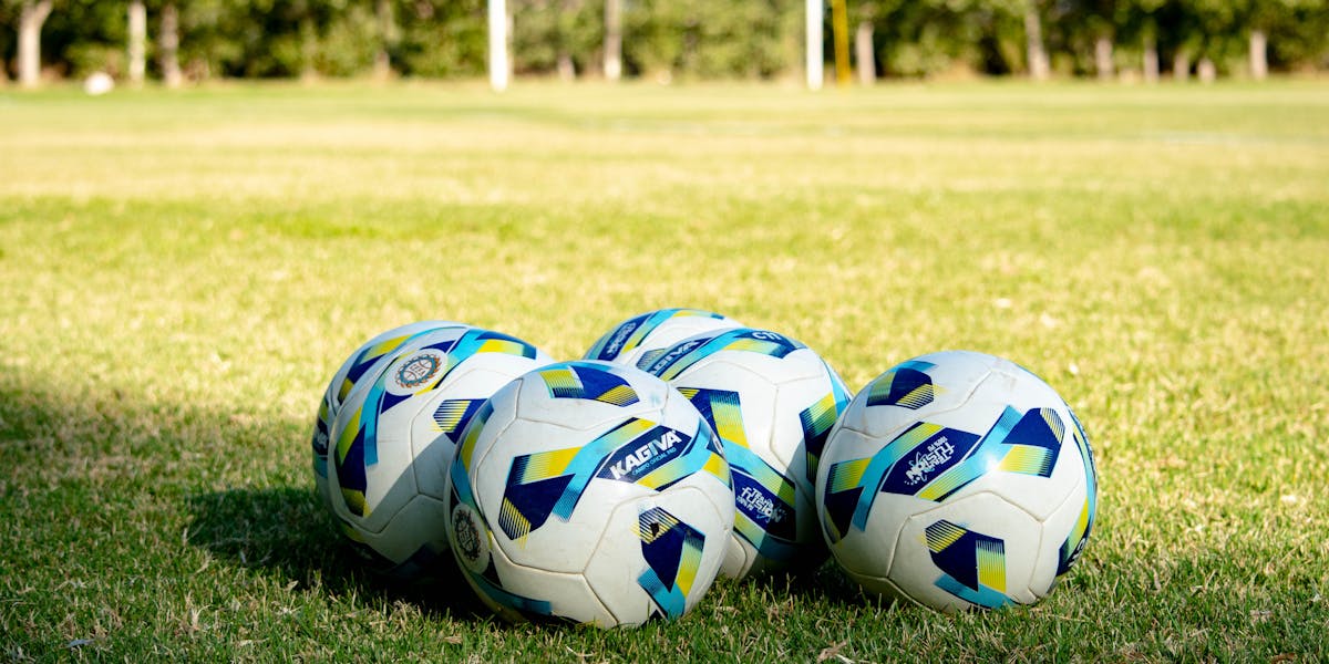 Group of soccer balls on a green grass field with a training cone, perfect for spo...