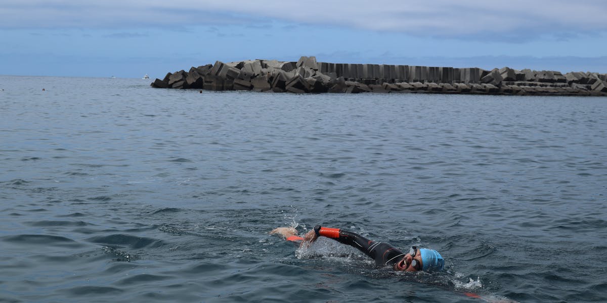 Man swimming in open sea near a coastal breakwater, showcasing recreational sport.