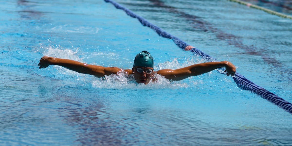 A swimmer executes a butterfly stroke in a turquoise outdoor pool.