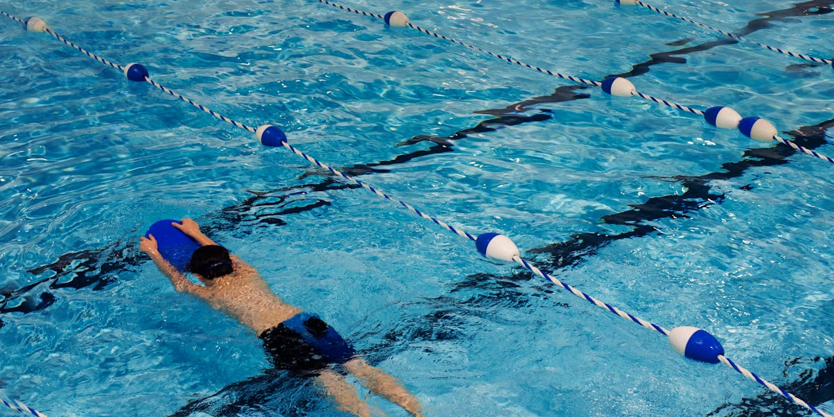 A young swimmer practicing with a kickboard in a swimming pool on a sunny day.