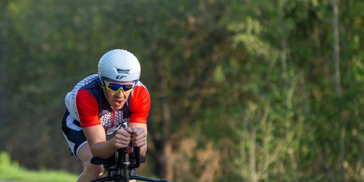 Triathlete cycling fast on a rural road during training, wearing a helmet and su