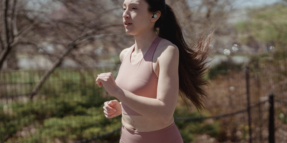 A woman jogs outdoors with wireless earbuds, embodying a healthy lifestyle.