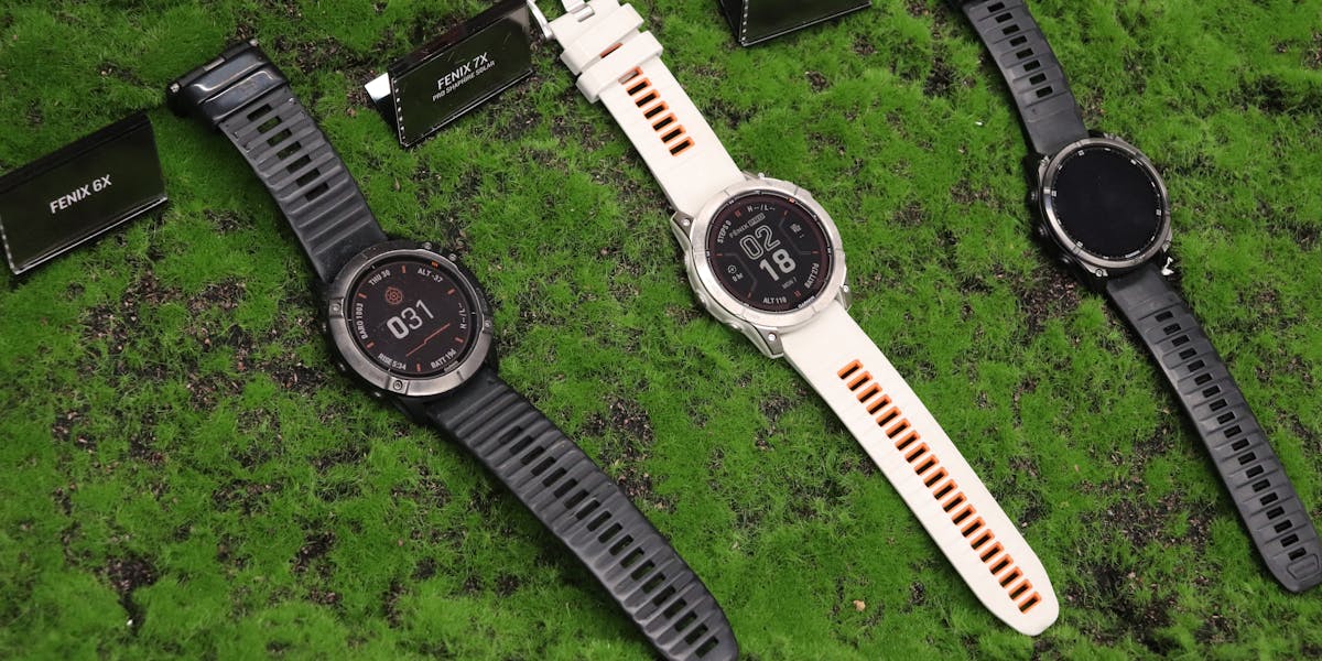 Three outdoor watches displayed on a textured green surface, featuring Fenix model...